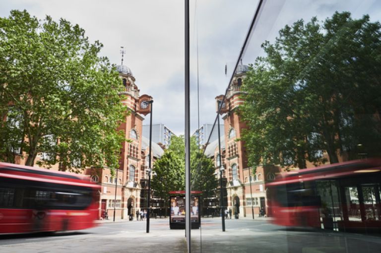 An image of Rhind Building (which is made of glass) reflecting College Building and the clocktower. A red London bus drives by