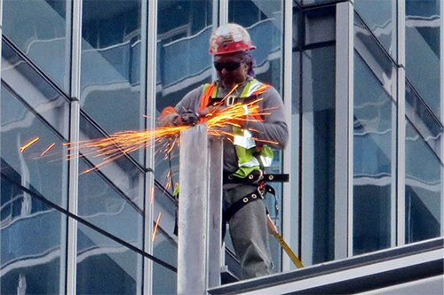 A construction worker in a safety harness does repair work on a high building